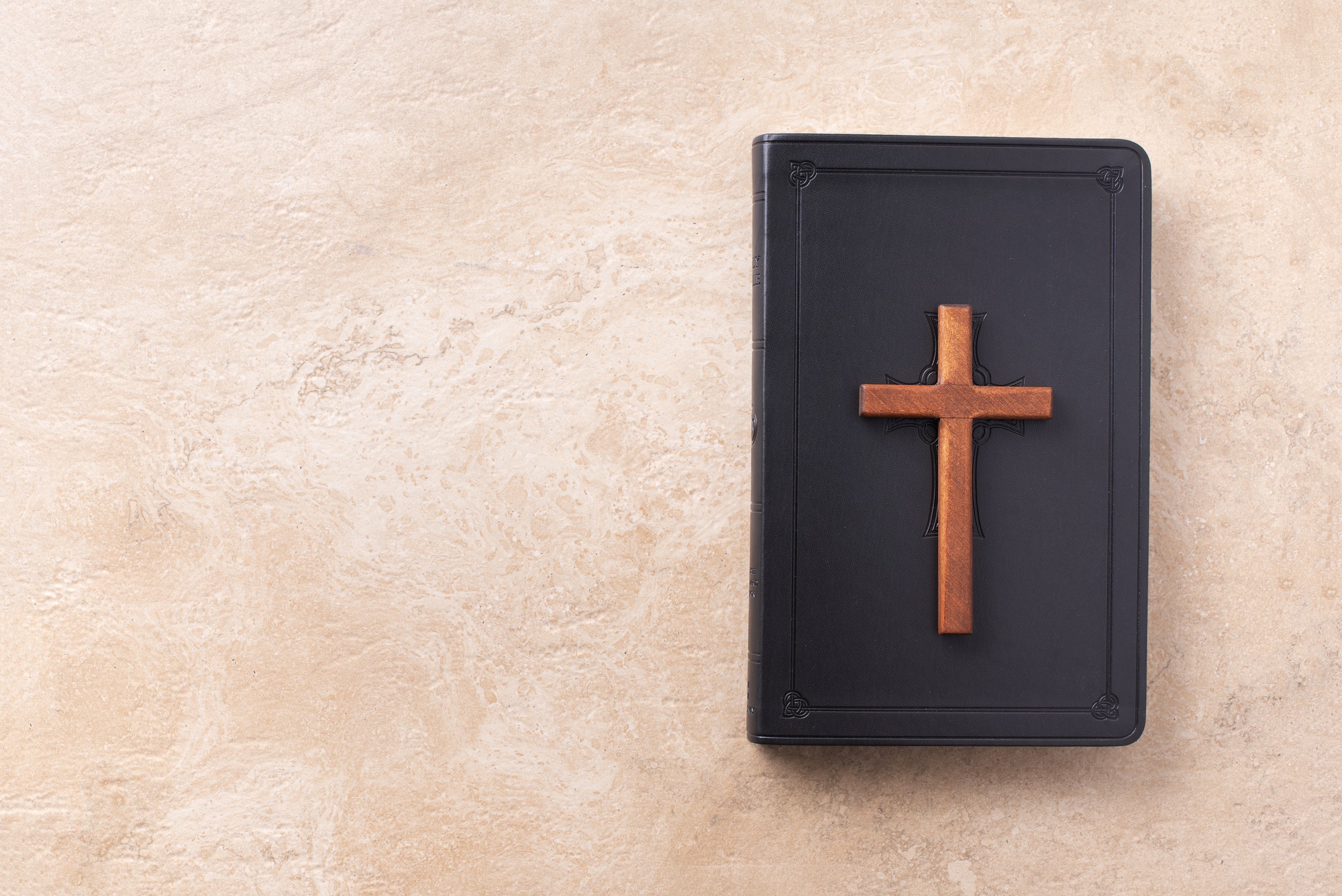 Wooden cross on Bible over marble background. Reminder of Jesus sacrifice and Christ resurrection